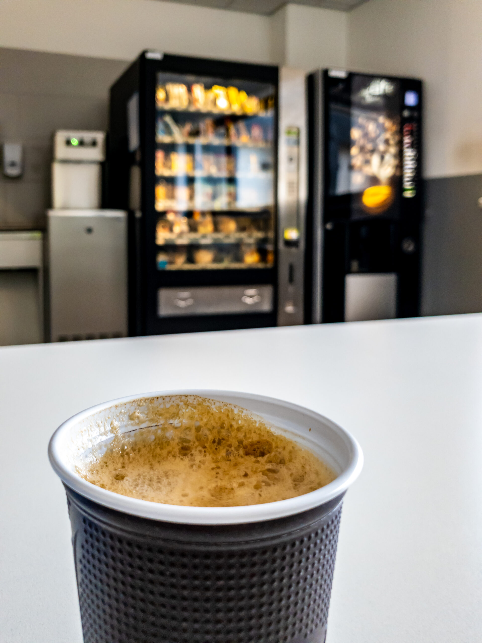 Bicchiere di caffè su un tavolo con distributori automatici sullo sfondo